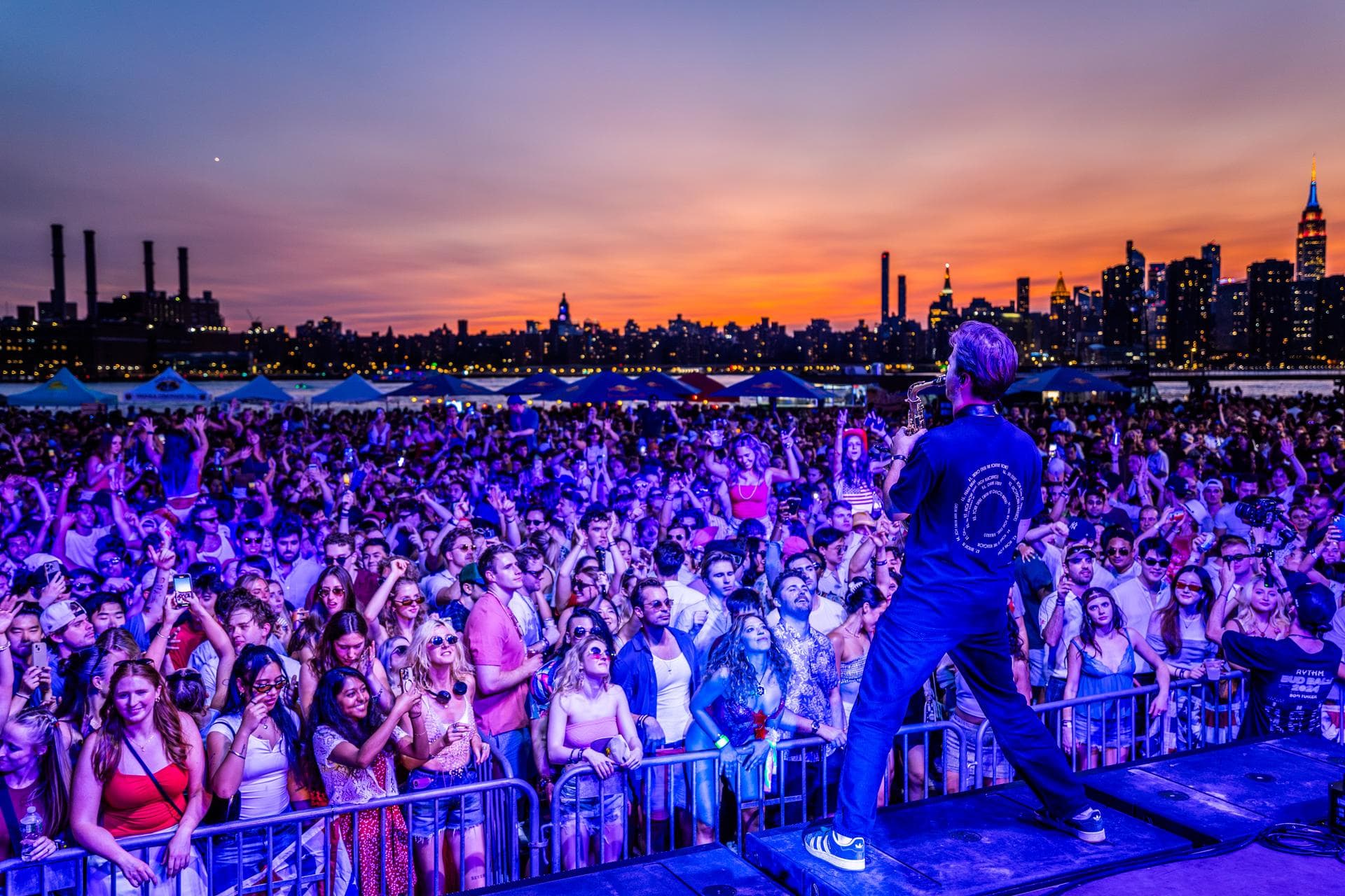 Performer on stage facing the crowd at sunset, NYC skyline behind