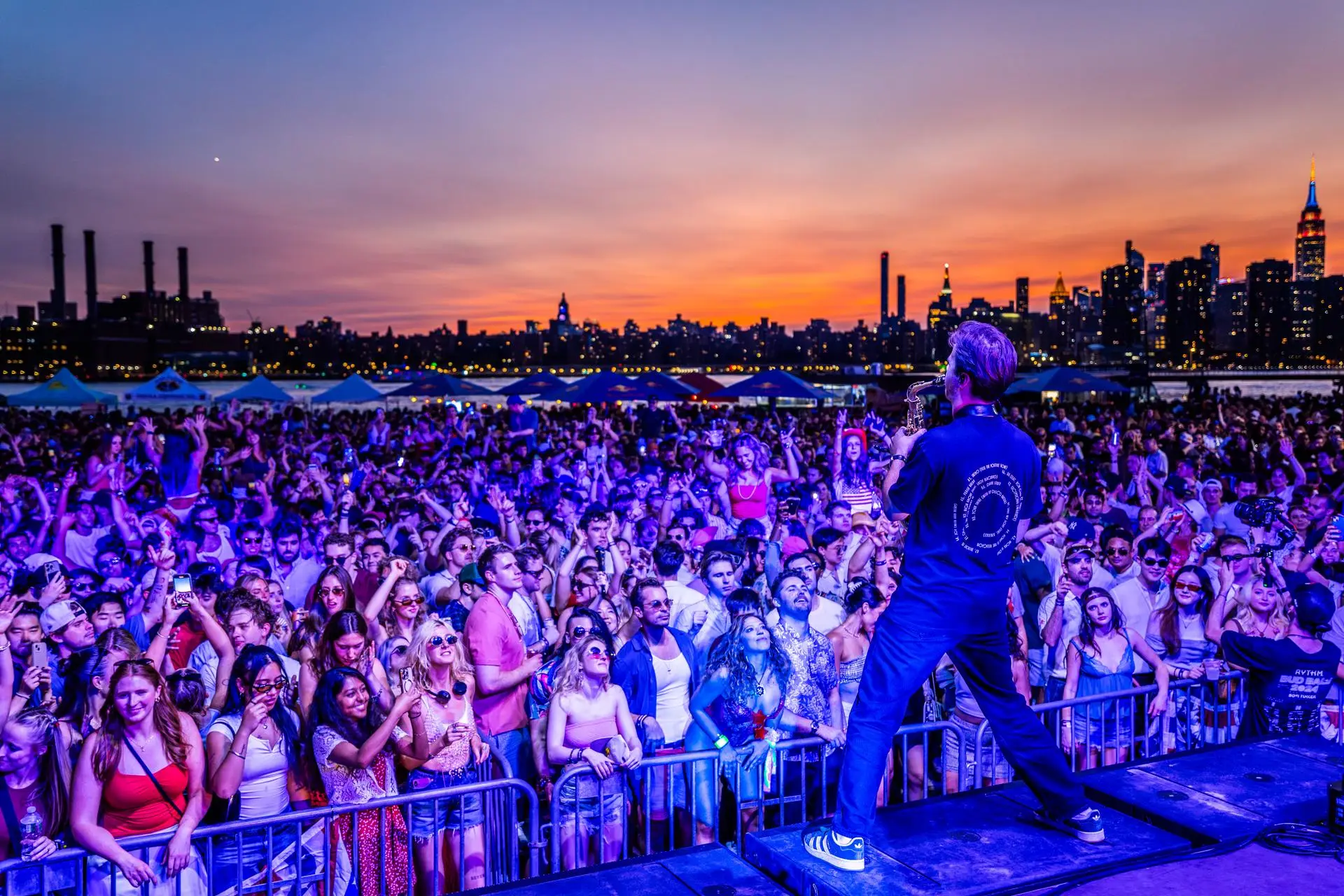 Performer on stage facing the crowd at sunset, NYC skyline behind